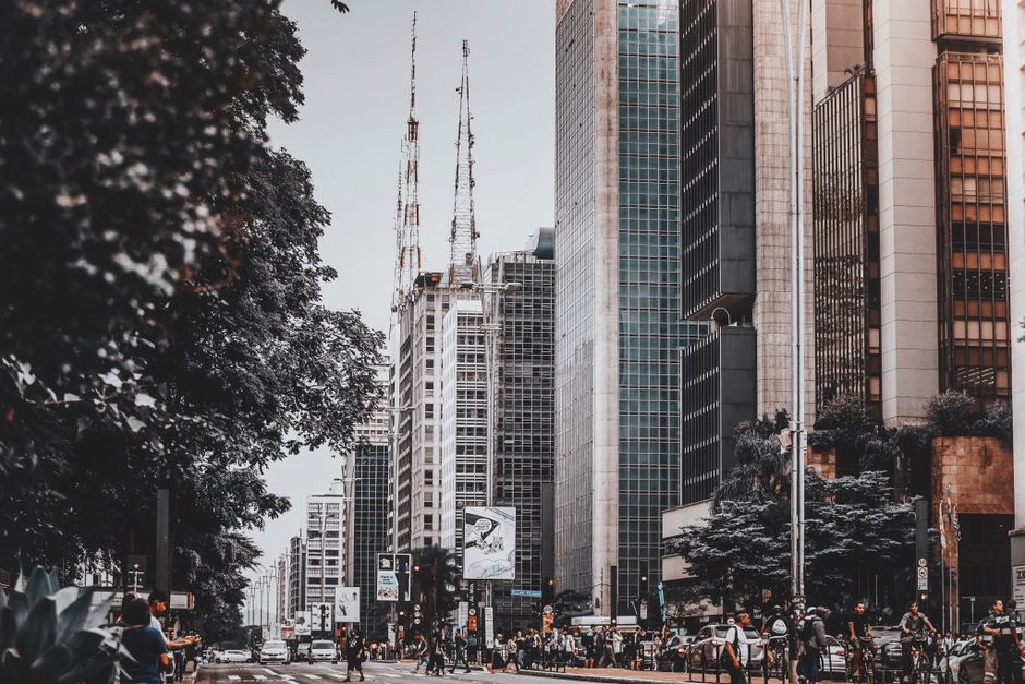 Foto ilustrativa de avenida movimentada com prédios altos e torres de antena em uma metrópole