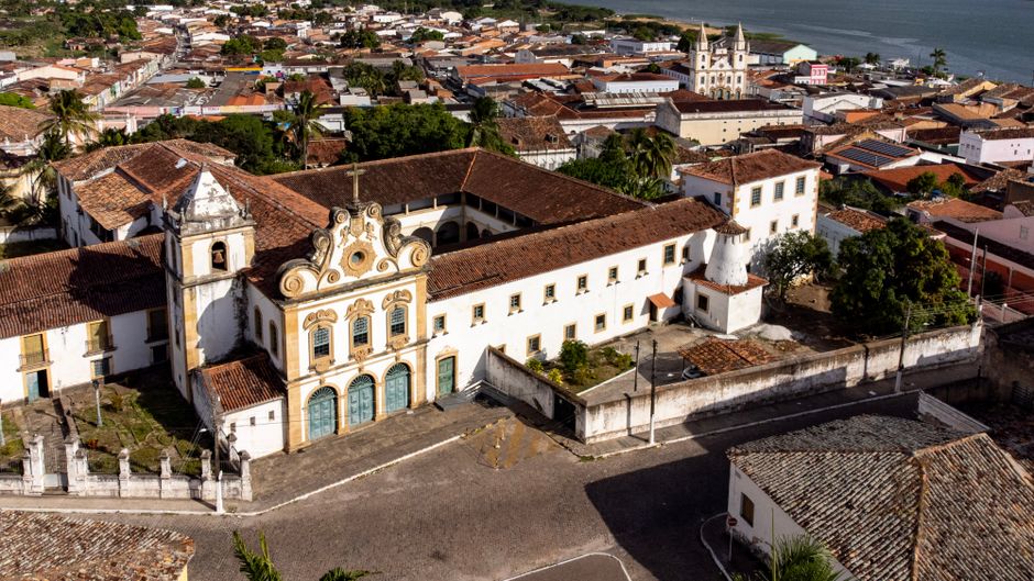 Foto ilustrativa de cidade histórica vista do alto, com igreja colonial e casas de telhado cerâmico