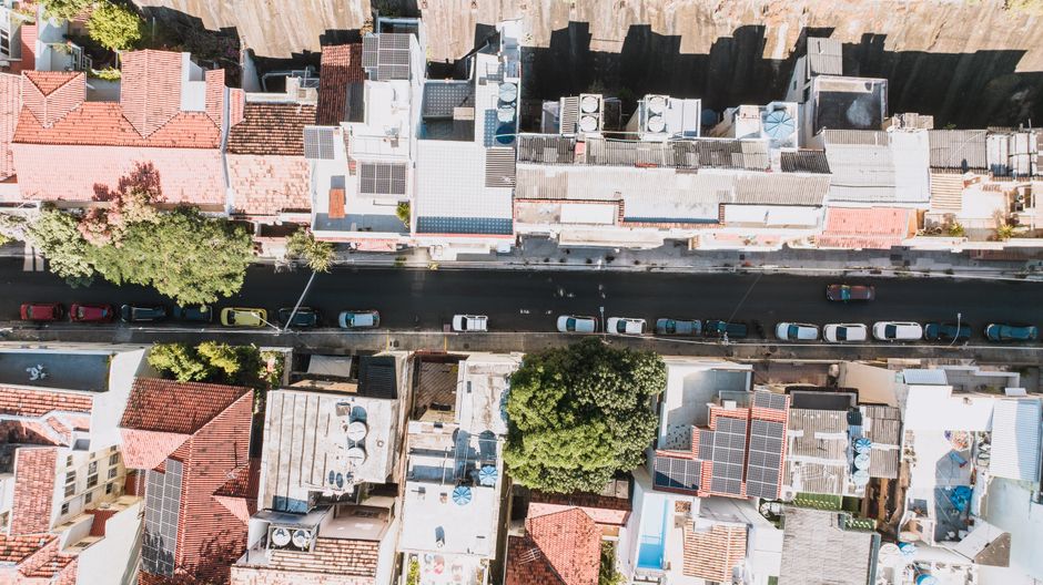 Vista aérea de uma rua com casas e prédios baixos, telhados com painéis solares e árvores