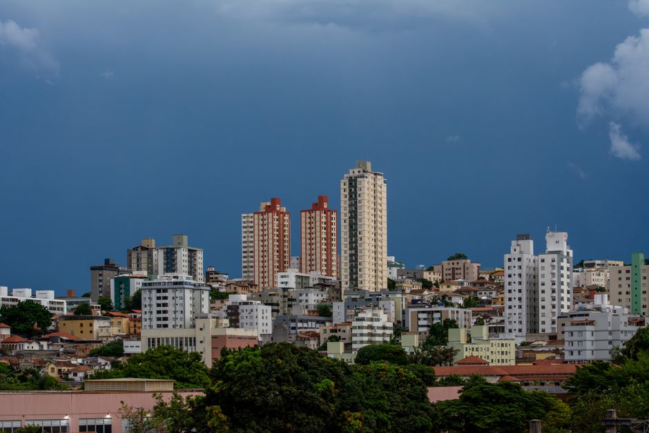 Foto ilustrativa de prédios residenciais em meio a casas e árvores sob céu nublado